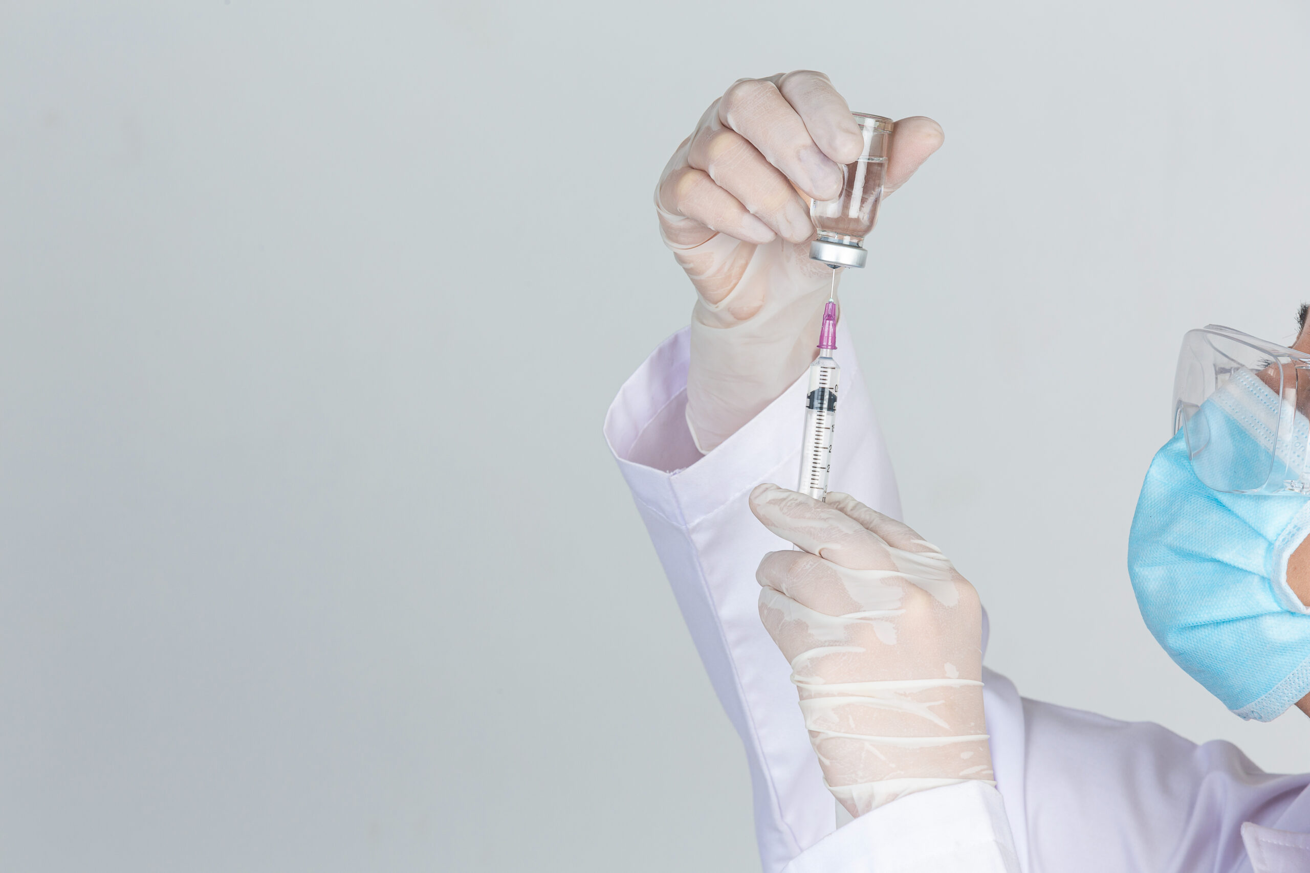 Young doctor is holding hypodermic syringe with vaccine vial